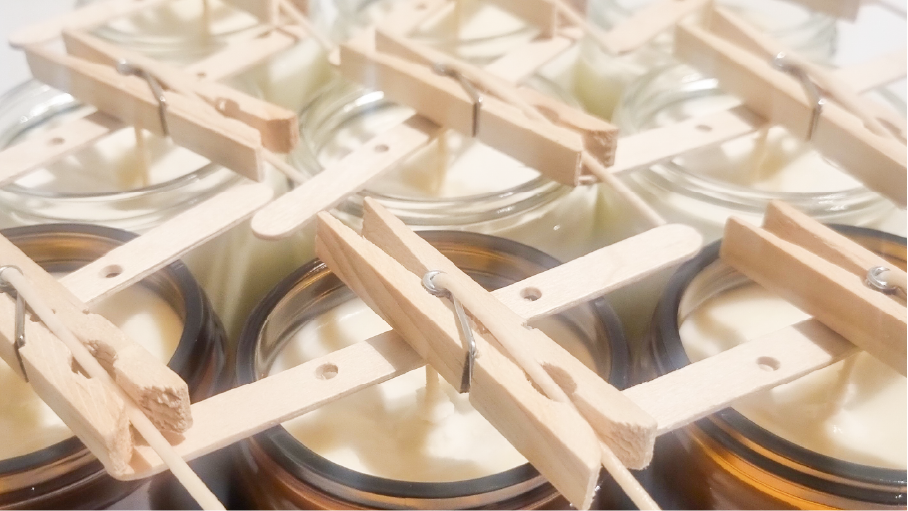 Soy wax candles curing with pegs holding wicks in place.