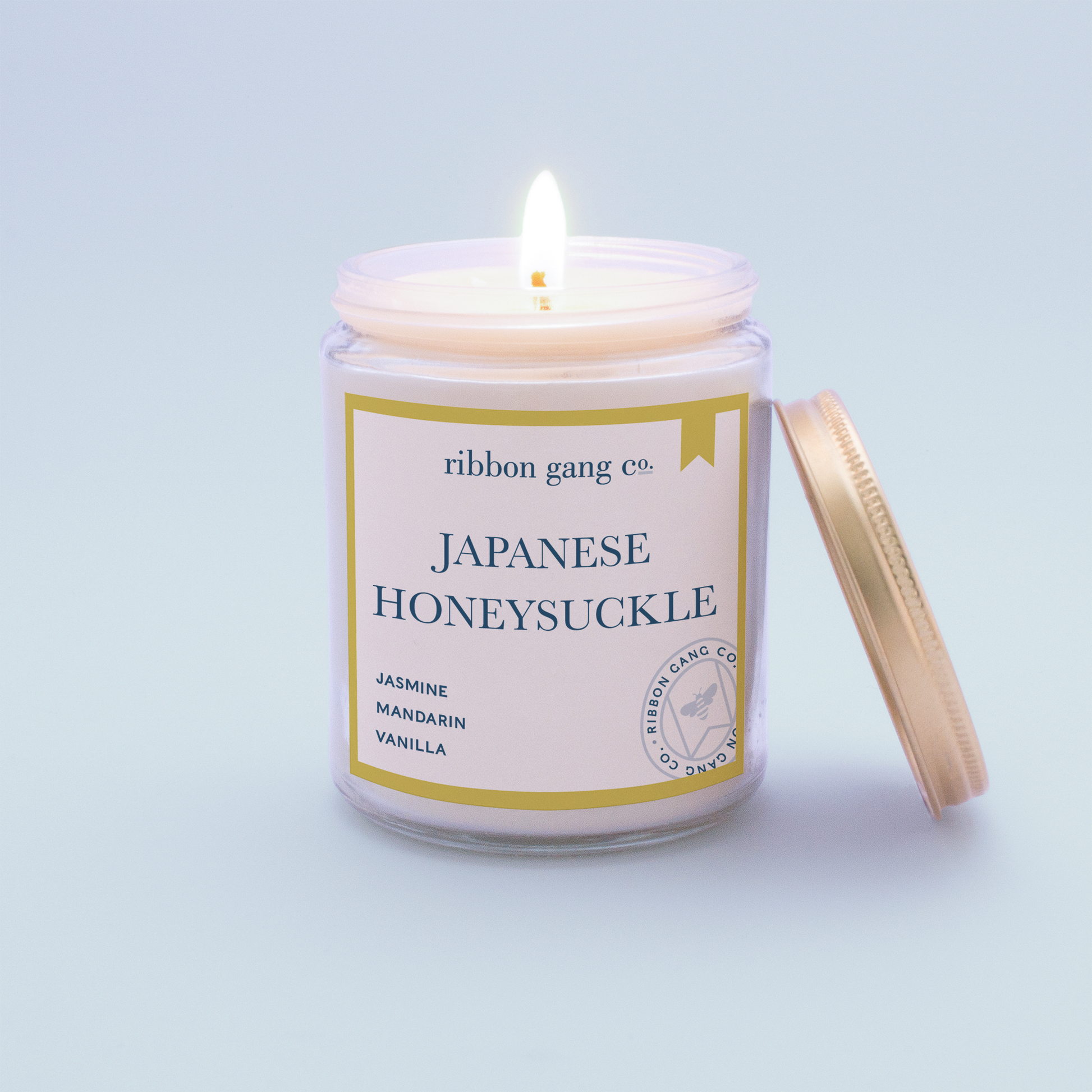 Japanese Honeysuckle Candle in a clear jar burning with a gold lid