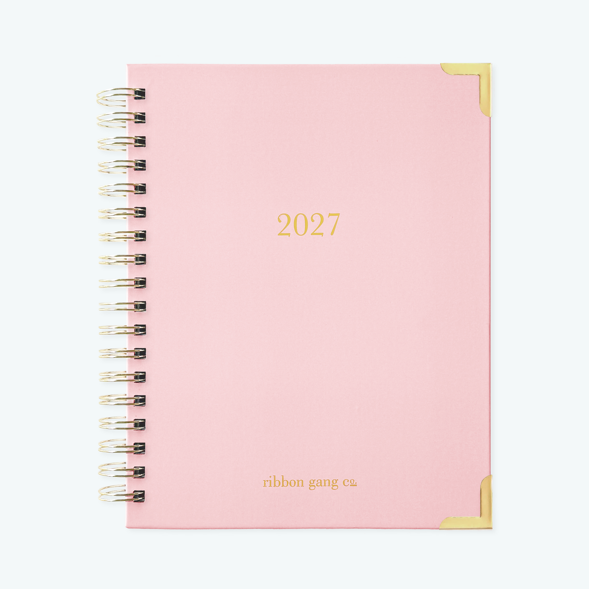 A blush pink spiral bound 2027 planner with gold lettering and gold corners on a white background.