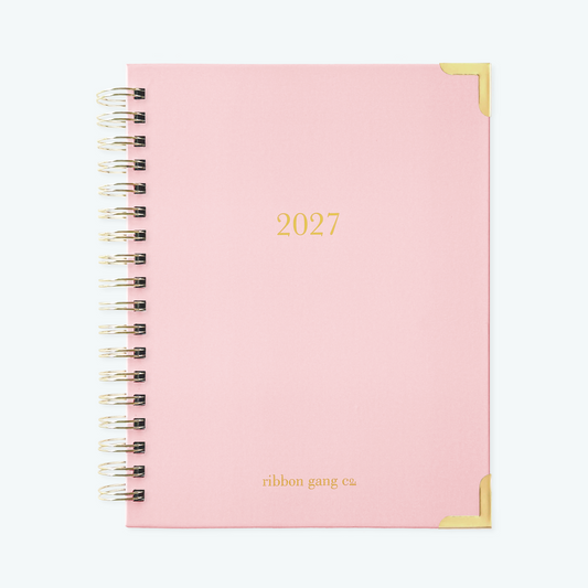 A blush pink spiral bound 2027 planner with gold lettering and gold corners on a white background.