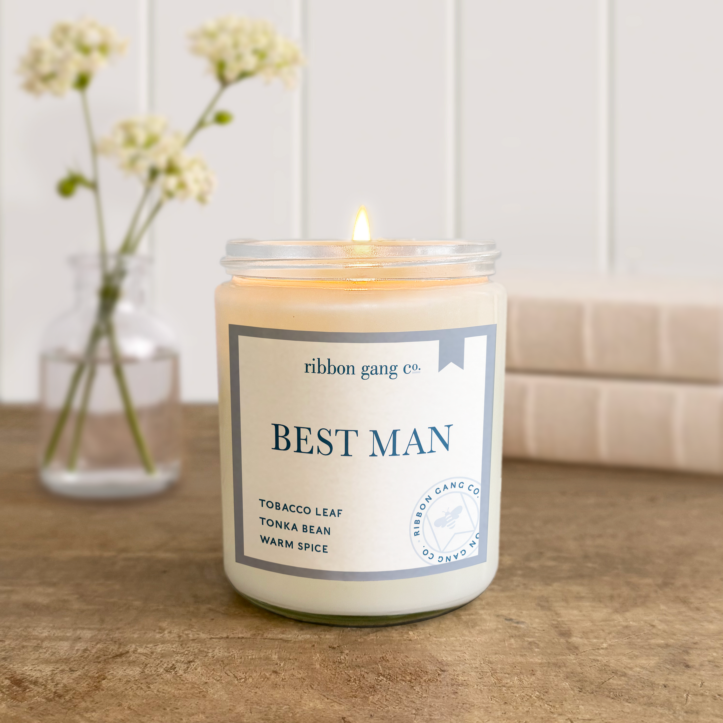 Candle labeled 'Best Man' by Ribbon Gang Co. on a wooden surface with a blurred background.