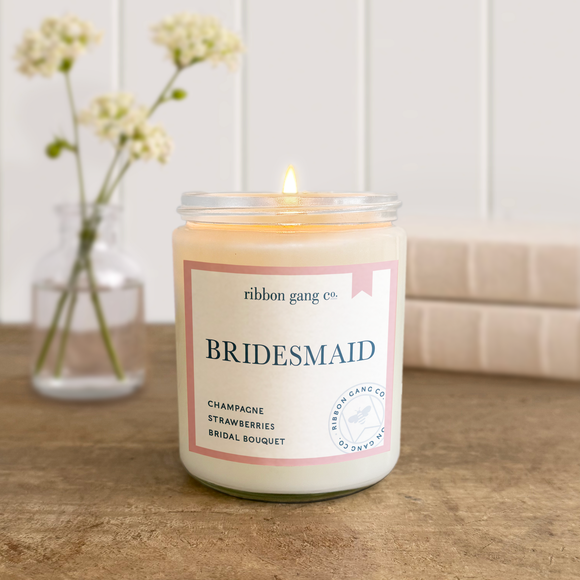 Candle labeled 'Bridesmaid' by ribbon gang co. on a wooden surface with a blurred background.