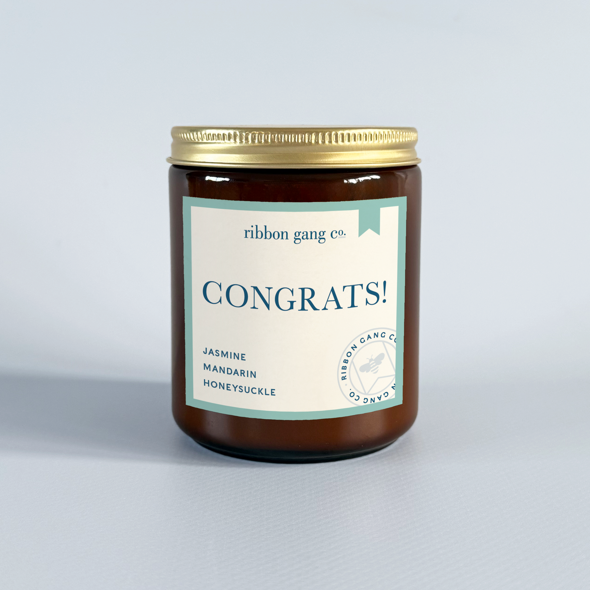 Candle with 'Congrats!' label by Ribbon Gang Co. on a light grey background.