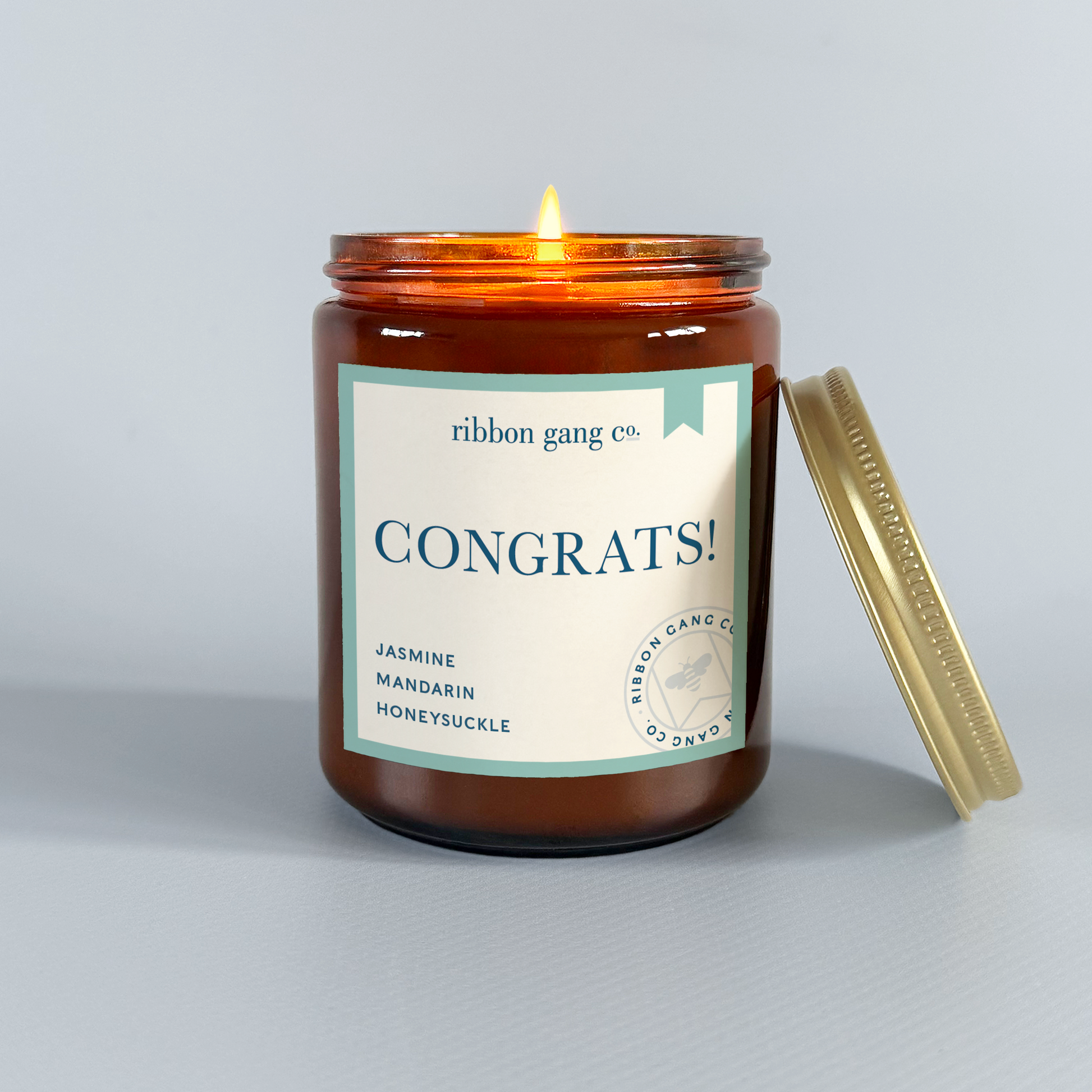 Candle in an amber jar with a 'Congrats!' label on a light grey background.
