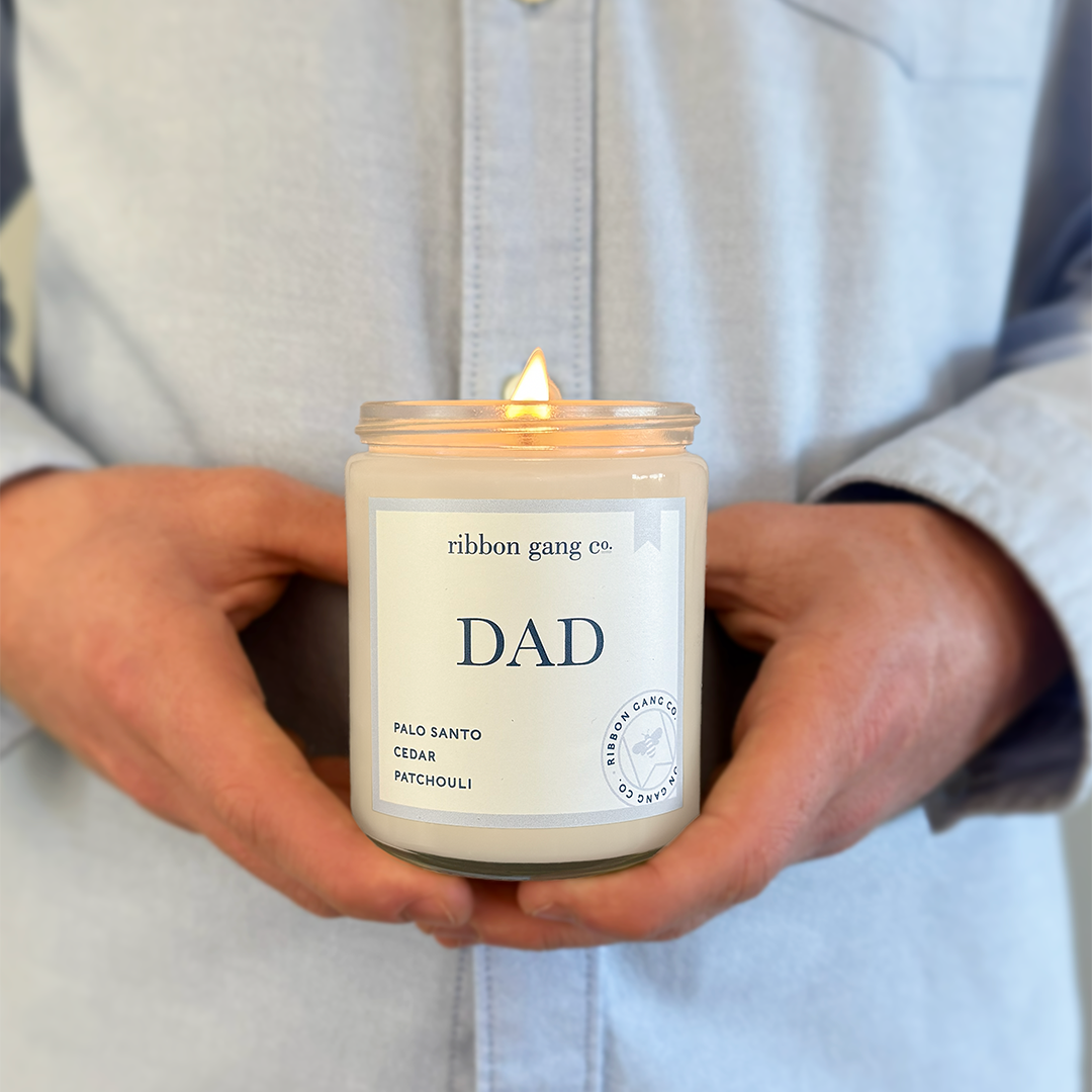 A man in a blue shirt holding a lit Dad candle in a clear jar.