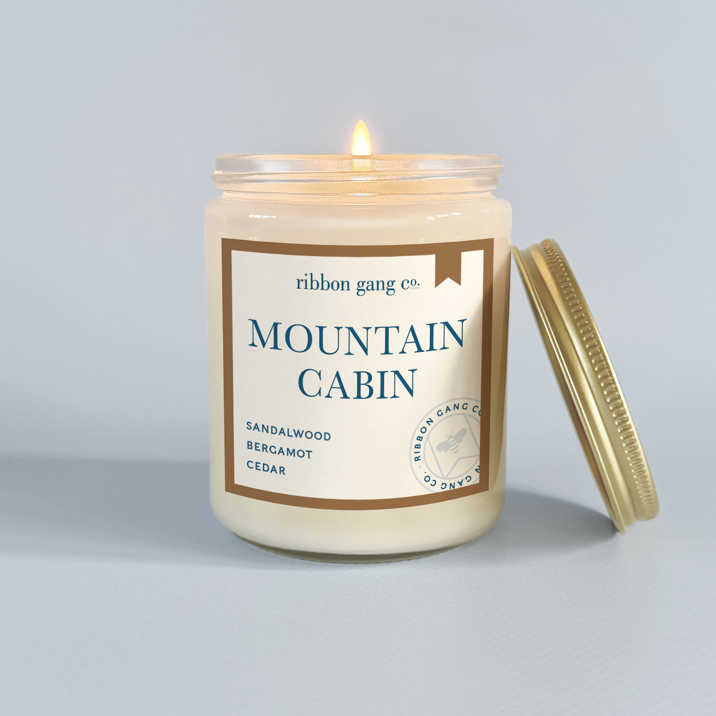 Candle in a jar labeled 'Mountain Cabin' by Ribbon Gang Co. on a light grey background.