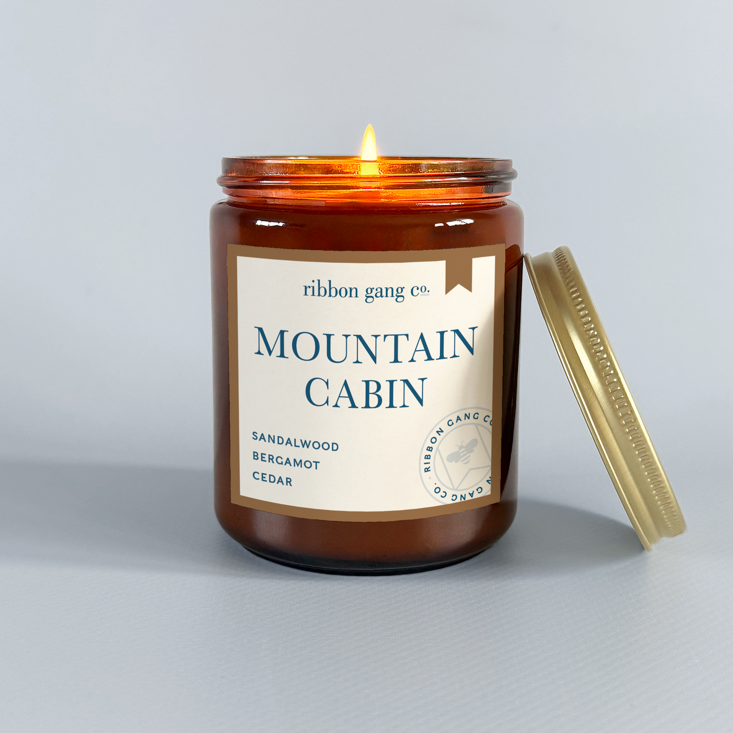 Candle in a brown jar labeled 'Mountain Cabin' by Ribbon Gang Co. on a light grey background.