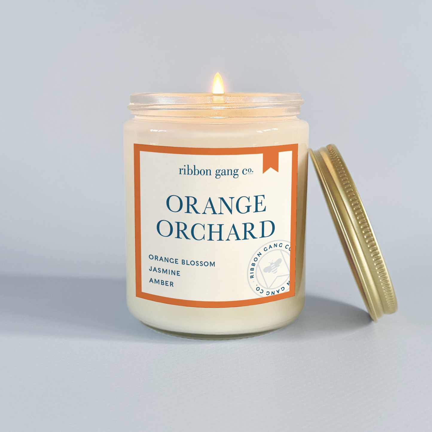 Candle labeled 'Orange Orchard' by Ribbon Gang Co. on a grey background.