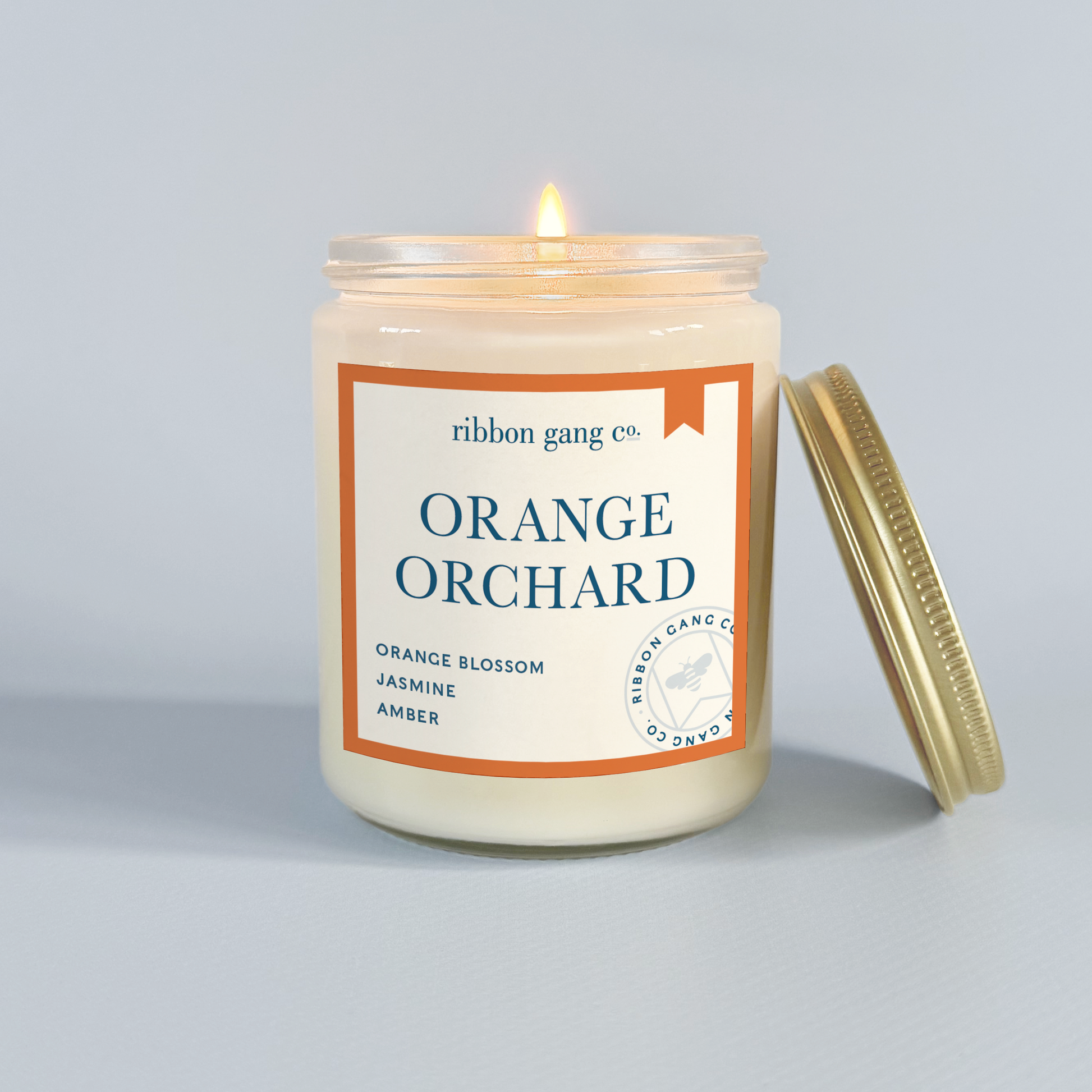 Candle labeled 'Orange Orchard' by Ribbon Gang Co. on a grey background.