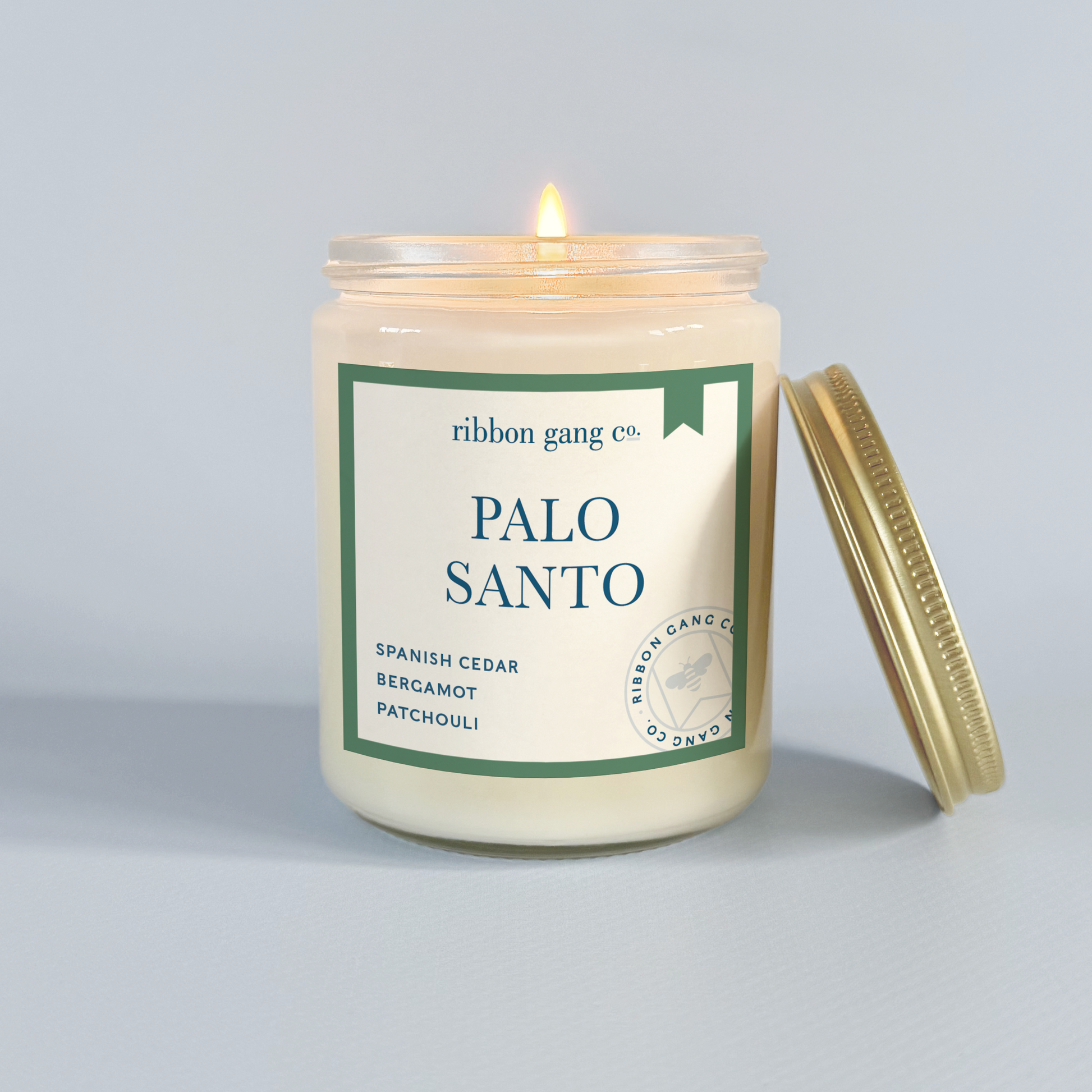 Candle with a label reading 'Palo Santo' by Ribbon Gang Co. on a light grey background.