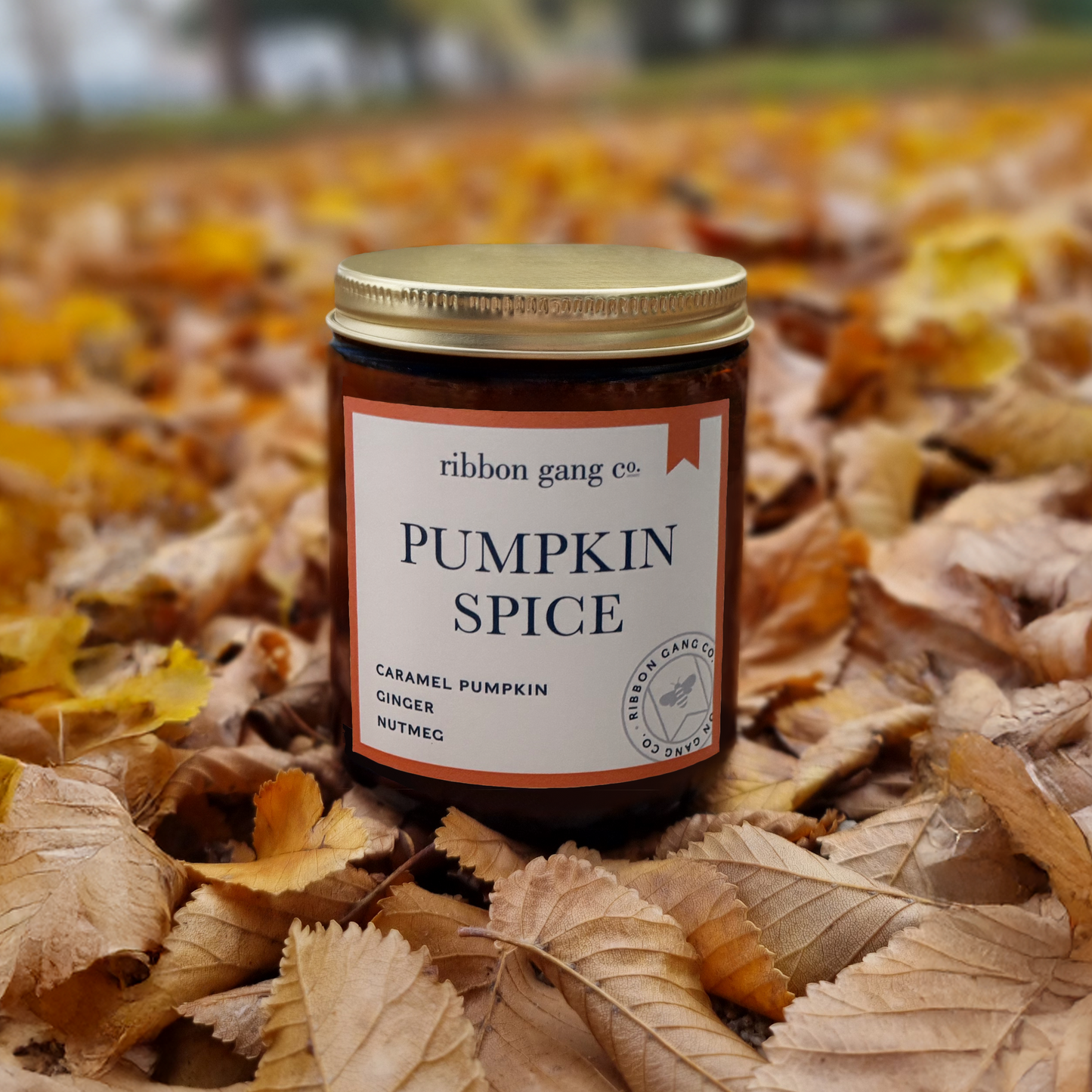 Jar of 'Pumpkin Spice' candle from Ribbon Gang Co. on a bed of autumn leaves.