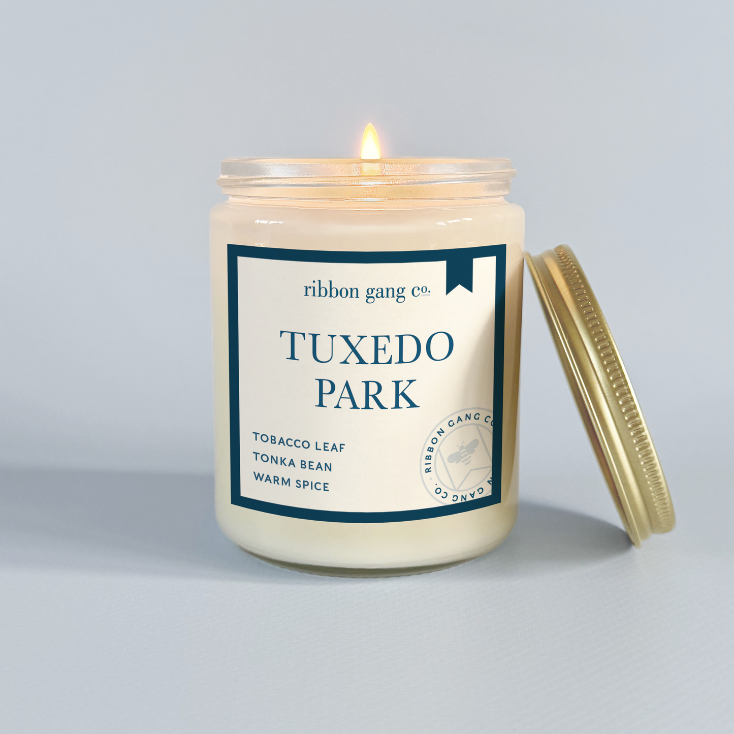 Candle in a jar labeled 'Tuxedo Park' by Ribbon Gang Co. on a grey background.