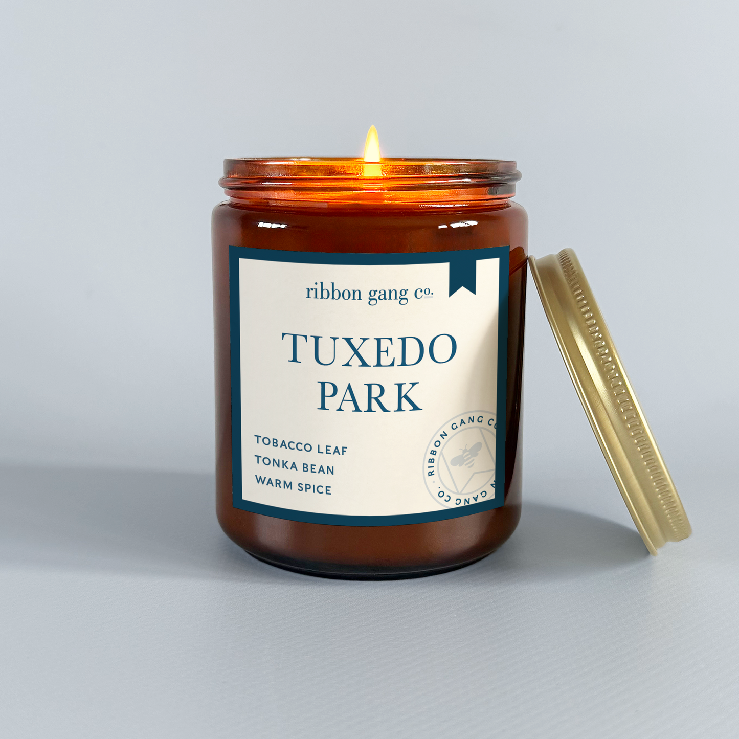 Candle in a jar labeled 'Tuxedo Park' by Ribbon Gang Co. on a grey background.